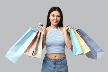 Fashionable young Asian woman in stylish denim skirt with shopping bags on grey background