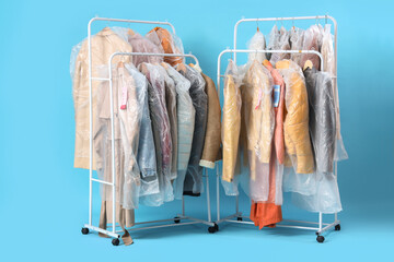 Racks with clothes in plastic bags after dry-cleaner's on blue background