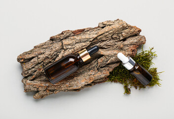 Tree bark, green moss and bottles of essential oil on white background, closeup