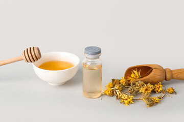 Bottle of essential oil, honey and dried flowers on white background, closeup