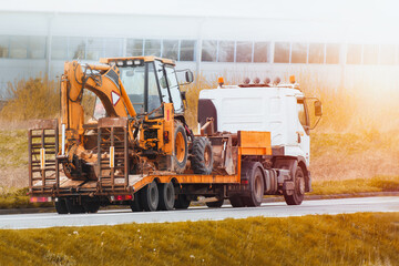 Flatbed Truck delivering heavy machinery to the construction site. Excavator tractor or crane. Construction industry.