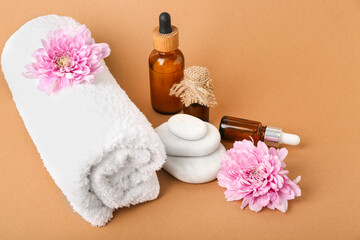 Bottles of floral essential oil, spa stones and towel on brown background