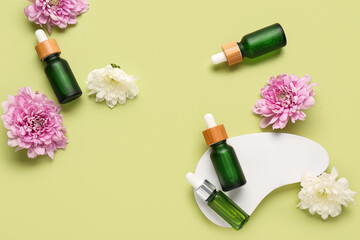 Bottles of essential oil, flowers and decor on green background