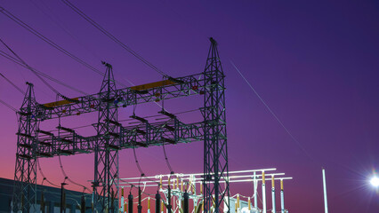 Silhouette of high voltage electric pylons with electrical equipment and insulators of power substation against twilight sky background