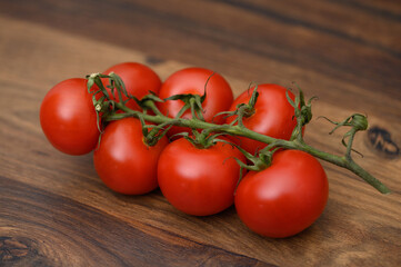 Piękne czerwone dojrzałe pomidory na gałązce na drewnianej desce  - obrazy, fototapety, plakaty