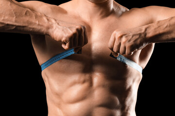 Male bodybuilder measuring his chest on black background, closeup