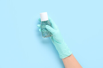 Female hand in gloves with bottle of sanitizer on blue background