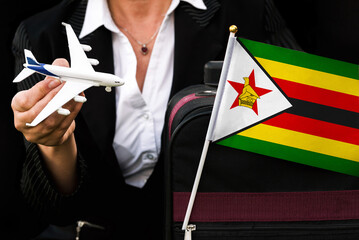 business woman holds toy plane travel bag and flag of Zimbabwe
