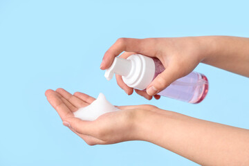 Female hands with bottle of sanitizer product on blue background