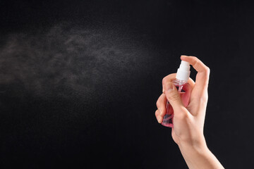 Woman spraying sanitizer on black background