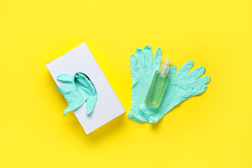 Bottle of sanitizer and rubber gloves pack on yellow background
