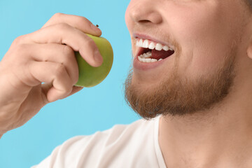 Young bearded man eating apple on blue background, closeup