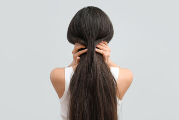Beautiful young woman with healthy long hair on grey background, back view