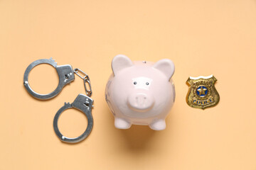 Piggy bank with handcuffs and police badge on orange background