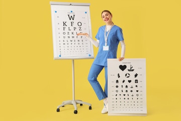 Female ophthalmologist with eye test charts on yellow background