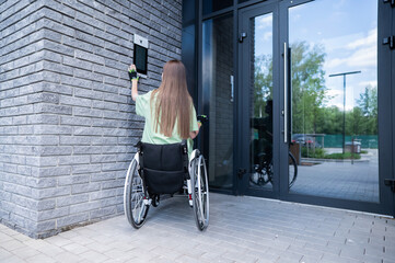A woman in a wheelchair with an assistive device for manual control enters the entrance. Electric hand bike.