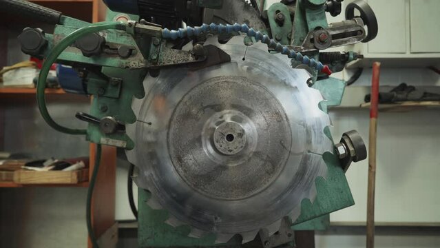 Automated Saw grinding machinery is used at an industrial woodworking factory. Grinding machinery is slowly sharpening the edges of the saw blade. Modern Industrial grinding machinery scraping the saw