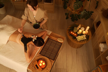 Beautiful Asian woman undergoing mud treatment on table in dark spa salon, top view