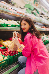Young Korean woman shopping without plastic bags in grocery store. Vegan zero waste girl choosing fresh fruits and vegetables in supermarket. Part of a series