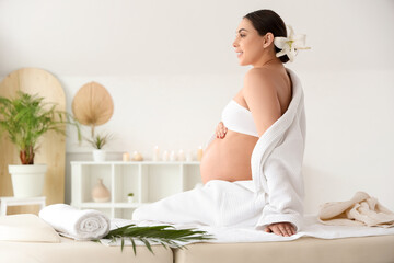 Young pregnant woman with lily flower sitting in spa salon