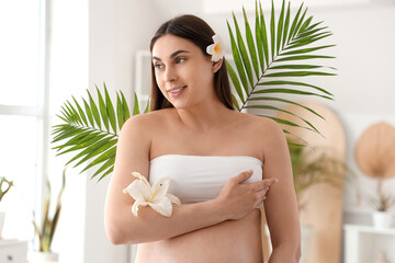 Obraz na płótnie Canvas Young pregnant woman with flowers and palm leaves in spa salon