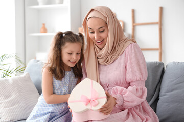 Little girl with her Muslim mother opening gift box on sofa at home