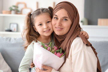 Little girl with tulips and her Muslim mother hugging at home, closeup