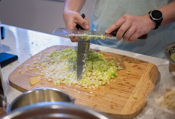 Hands of a man chopping cabbage using two knives in the home kitchen.