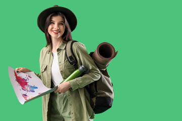Beautiful young happy female tourist with backpack, thermos and world map on green background