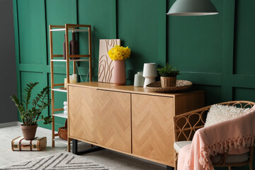 Interior of green living room with armchair, chest of drawers and vase of narcissus flowers