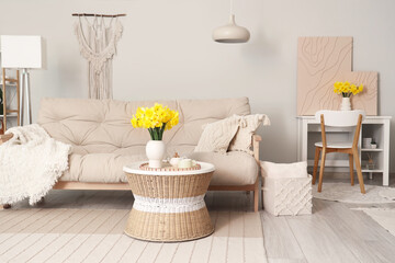 Stylish living room with cozy sofa, coffee table and bouquet of narcissus flowers