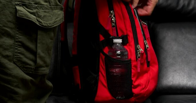 a man puts a bottle of water in the side pocket of a red backpack