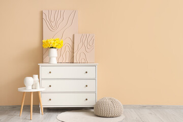 Chest of drawers with pictures and bouquet of narcissus flowers in beige room