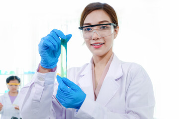 Beautiful Asian scientist woman in lab coats with safety glasses holding test tube with green...