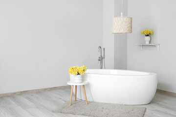 Beautiful vase with narcissus flowers on coffee table near bathtub in bathroom