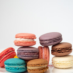 Close up delicious macaroon cookies in fresh mint green vanilla beige chocolate brown orange and pink colors. Light background, square frame. Contrast bright combination, bakery culinary.