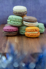 Close up delicious macaroon cookies in fresh mint green vanilla beige chocolate brown orange and pink colors. Blue bokeh shining blurred foreground decor. Contrast bright combination, bakery culinary.