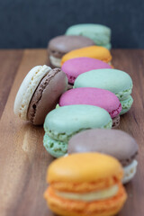 Close up delicious macaroon cookies in fresh mint green vanilla beige chocolate brown orange and pink colors. Shallow depth, vertical frame, wooden table. Contrast bright combination, bakery culinary.