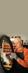 Old bike mechanic holding wheel in bicycle repair shop.