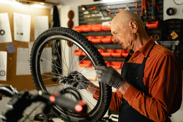 Elderly male mechanic repairing a bicycle in a workshop, holding a bicycle wheel in his hands, concentrated on work