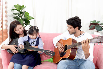 Happy Asian family. Chubby little girl daughter learning to play acoustic guitar with her dad....