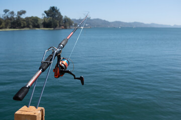 Fish rod mounted on a wooden spring rod holder with blurred background of water and landscape on horizon