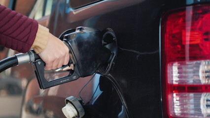 Hand with a gun to refuel the car. A woman fills her car