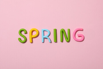 The word "spring" is made of colored plasticine, laid out on a pink background.