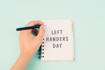 Left handers day is standing on a notebook, writing with the left hand, pen and table
