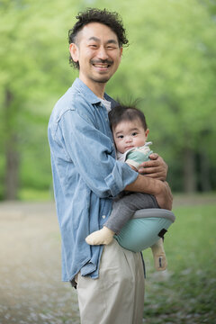 Dad holding a baby in the fresh green outdoors Image of ikumen or male childcare and parenting Looking at the camera