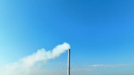 The sky turns hazy as an industrial facility releases white smoke, symbolizing the growing environmental and health challenges we face. Pollution and environment concept. Bird's eye view by drone.

