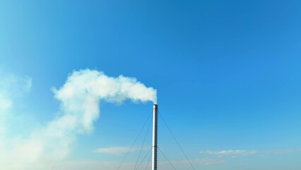 A factory emits thick white smoke, polluting the clear blue sky, highlighting the urgent need for cleaner industry practices. Health impacts and emissions concept. Bird's eye view by drone. 
