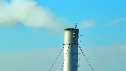 The towering industrial facility dominates the skyline, its relentless white smoke merging with the...