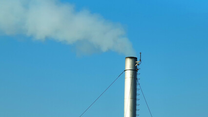 Thick white smoke spews from an industrial facility, tainting the blue sky, highlighting the urgent...